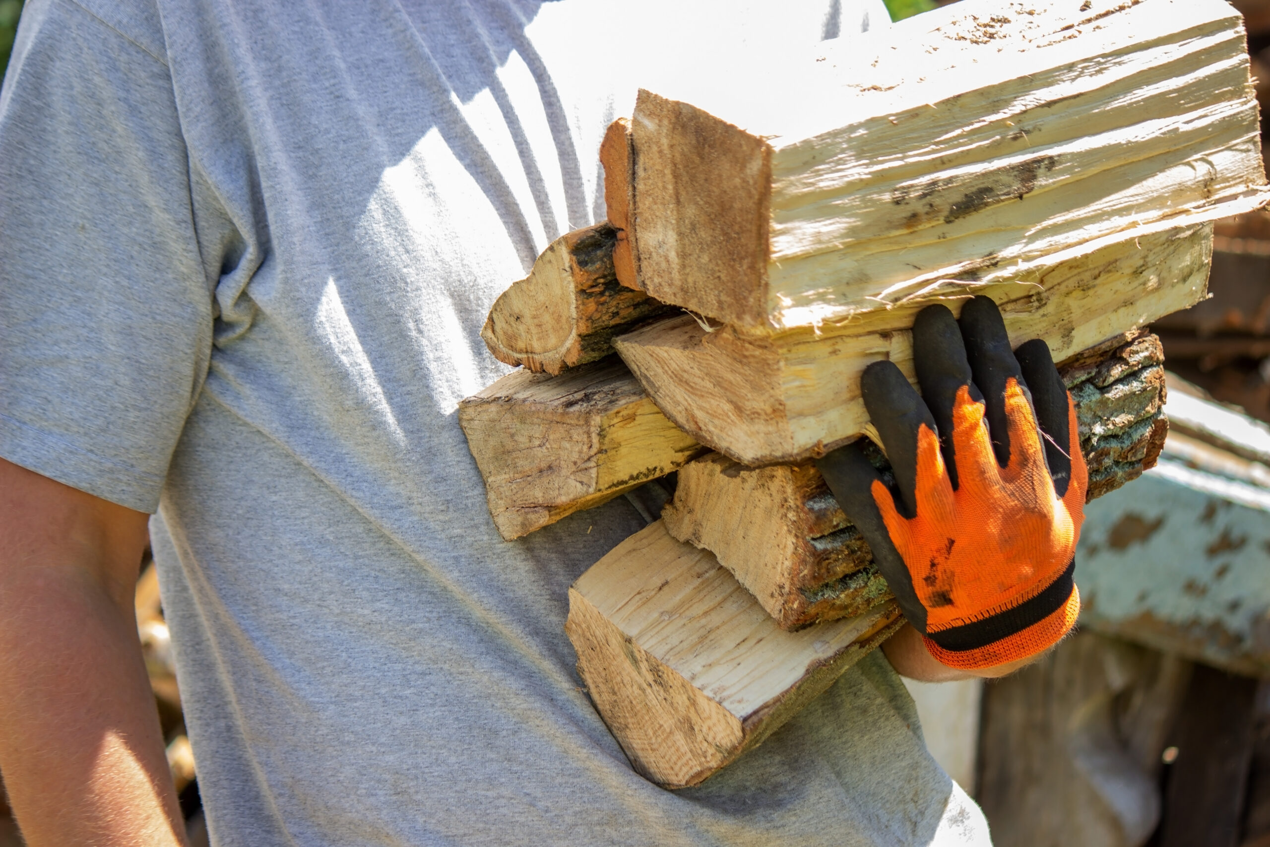 Man with orange and black gloves carrying firewood