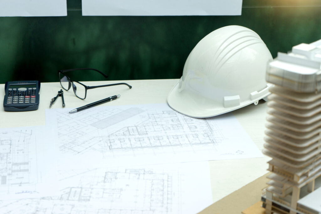 Table with plans for new construction surrounded by hard hat, office supplies, and project model